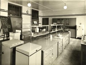Black and white photograph of a teaching kitchen with electric cooker and fridge