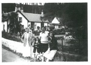 Photograph of man, woman and two children standing outside of a house