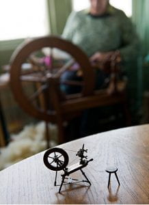 Photograph of a model spinning wheel with a person spinning on a wheel in the background