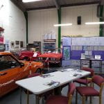 Photograph showing exhibition banners and table next to vintage cars