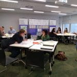 Photograph of a workshop session with people working round tables and exhibition banners in the background