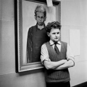 Alasdair Gray standing in front of painting of himself by Alan Fletcher